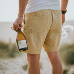 Mann steht am Strand und hält Limoni Spritz Flasche in der linken Hand und 2 Gläser in der rechten Hand